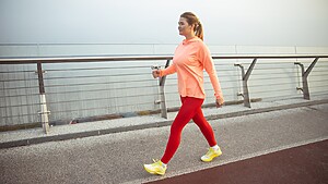 Woman walking outdoors on a waterfront path in athletic clothes during a low-impact fitness workout.