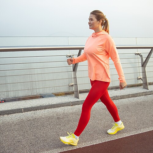 Woman walking outdoors on a waterfront path in athletic clothes during a low-impact fitness workout.