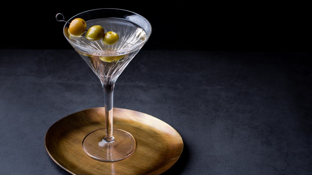 Dirty gin martini with green olives served in a coupe glass on a dark table.