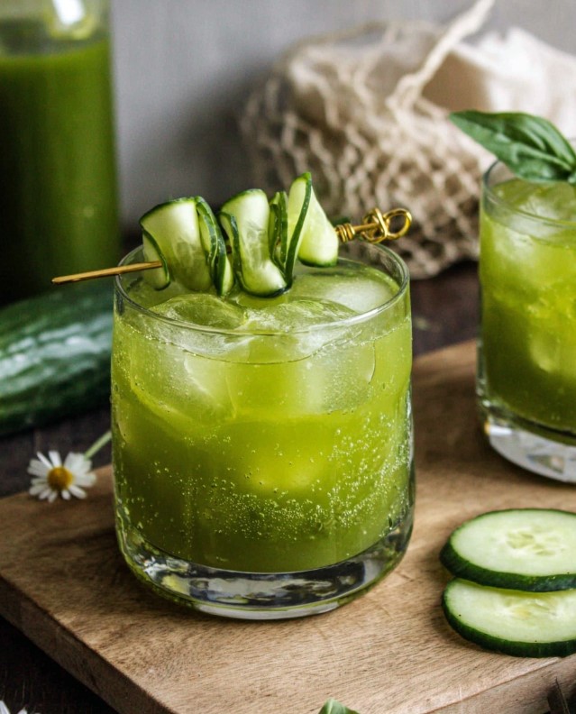 Green sparkling cucumber and basil drink served in a glass with ice cubes and garnished with cucumber slices, showing the final recipe