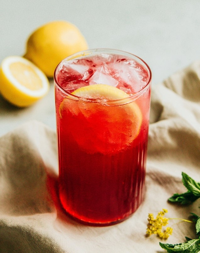 A glass of iced hibiscus lemonade garnished with a lemon slice, showing the final chilled drink ready to serve.