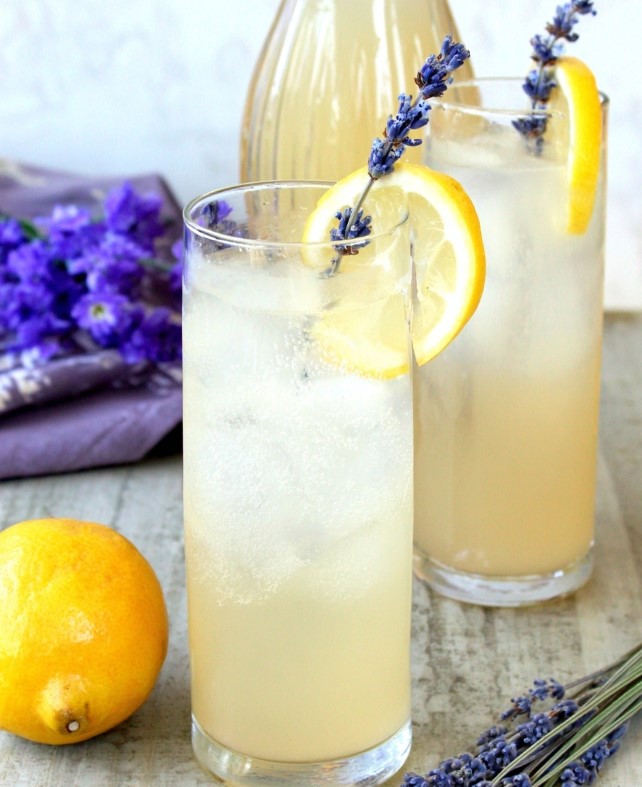 A glass of sparkling iced lemonade decorated with a lemon slice and a lavender sprig, representing the final serving stage after mixing the lemonade, cooling it, and adding ice.