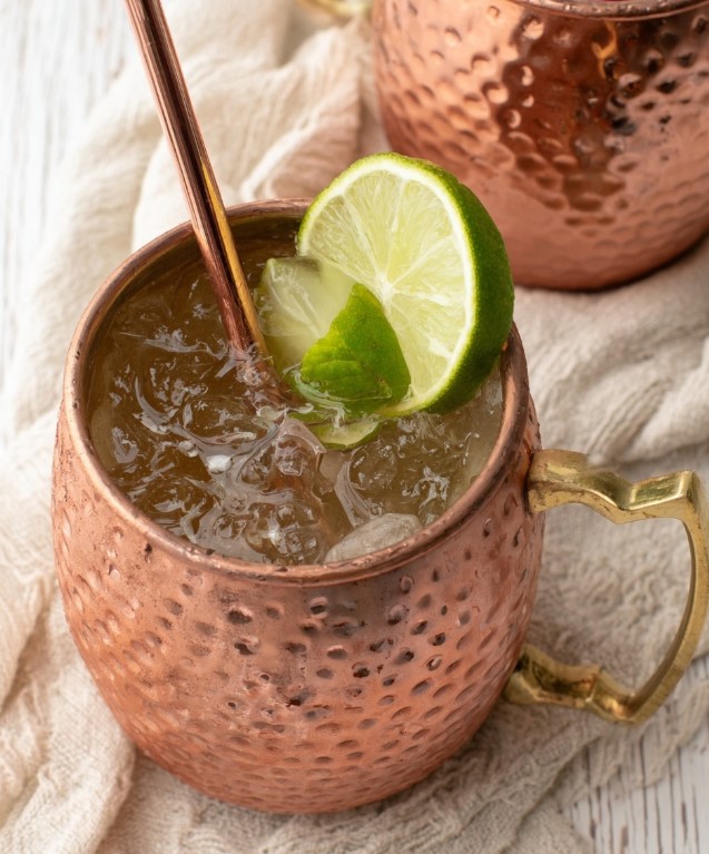 A copper mug filled to the brim with ice, holding a bubbly sugar-free Moscow Mule, garnished with a fresh lime wheel and mint sprig.
